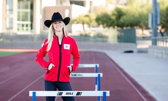 Portrait of Sage Watson standing on running track with hurdles.